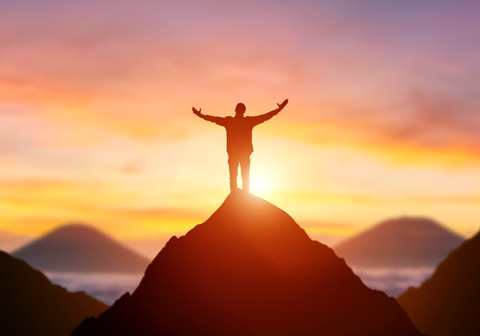 Silhouette of a business person on the top of a mountain peak in sunset background. Winner and conquer of businessman concept.